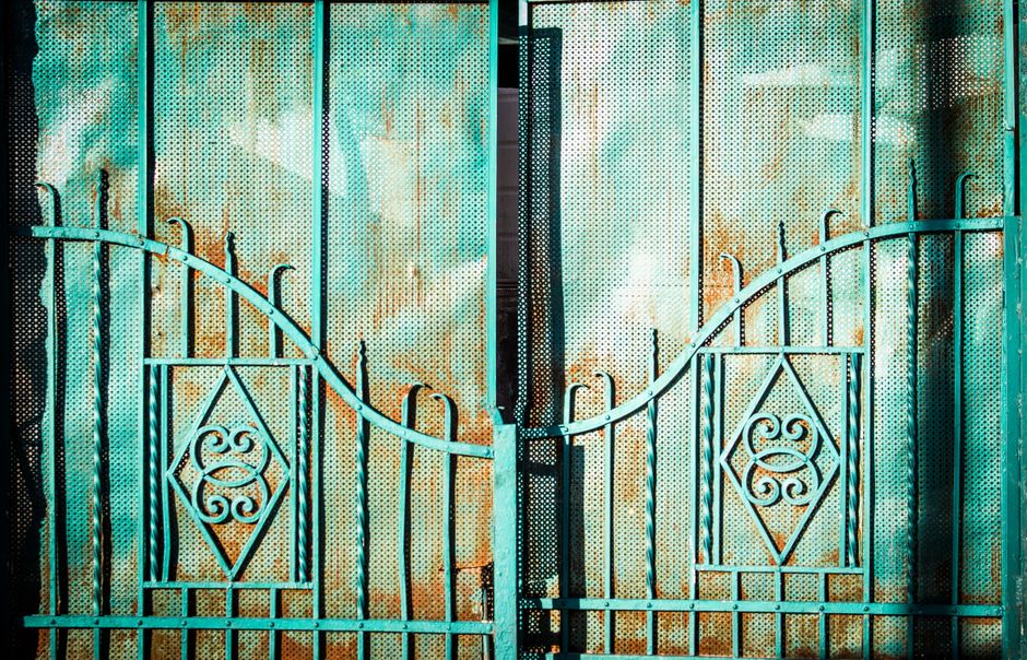 A rustic turquoise metal gate with intricate decorative patterns.