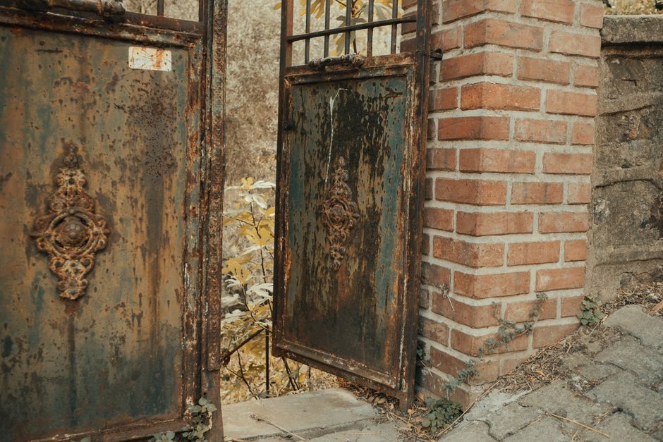 A vintage rusty metal gate set against a classic brick wall, offering a glimpse into a hidden garden.